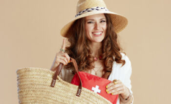Reiseapotheke - Eine junge Frau ist sommerlich bekleidet und trägt eine Tasche mit einem Erste Hilfe-Set für ihre Reise.